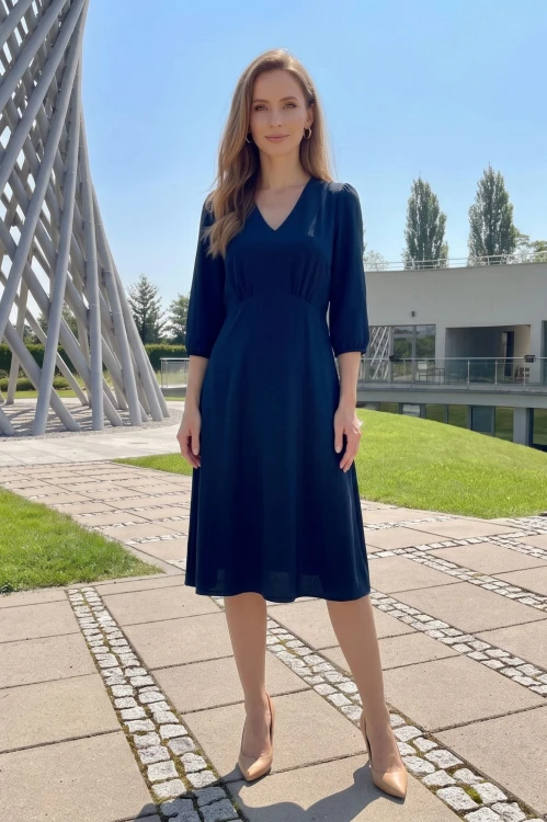 Na modelce, granatowa sukienka, o długości za kolana, lekko rozkloszowana, z odcięciem pod biustem w kształcie trójkąta, z lekkim przymarszczeniem, dekolt w literkę v, rękaw o długości 3/4 zakończony gumką.