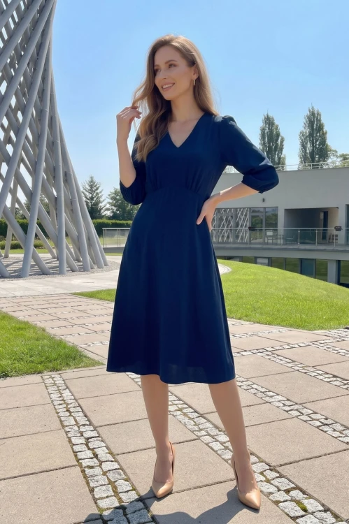 Na modelce, granatowa sukienka, o długości za kolana, lekko rozkloszowana, z odcięciem pod biustem w kształcie trójkąta, z lekkim przymarszczeniem, dekolt w literkę v, rękaw o długości 3/4 zakończony gumką.