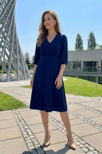 Na modelce, granatowa sukienka, o długości za kolana, lekko rozkloszowana, z odcięciem pod biustem w kształcie trójkąta, z lekkim przymarszczeniem, dekolt w literkę v, rękaw o długości 3/4 zakończony gumką.
