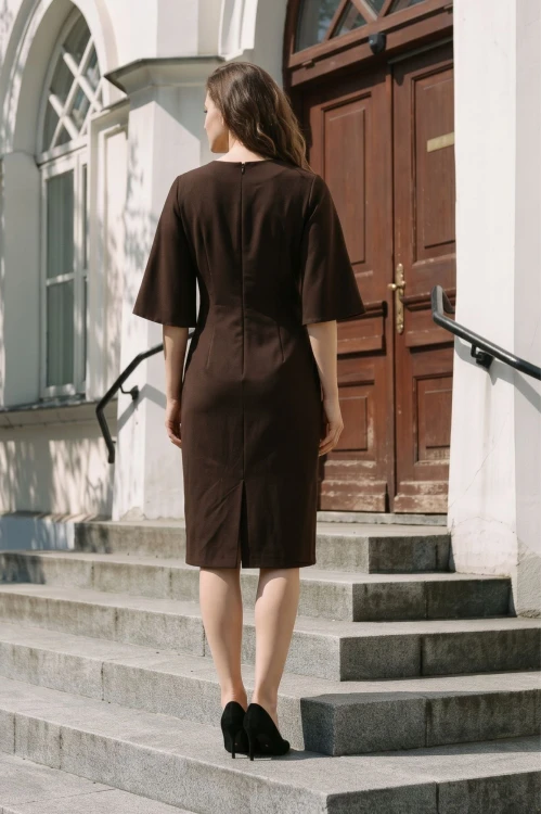 Na modelce stojącej tyłem, sukienka w kolorze brązowym, o długości do kolan, z rozporkiem, dekolt w literkę v, rękaw o długości 3/4 rozszerzany, zapinana na długi kryty suwak, zaszewki modelujące,