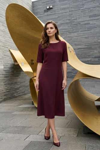 Na modelce stojącej przodem, sukienka midi w kolorze burgundowym, z obniżoną talią, niewielki okrągły dekolt, rękawek kimonowy o długości do łokcia, dół sukienki  rozkloszowany