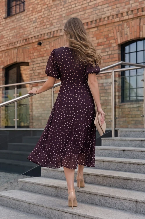 Na modelce stojącej tyłem elegancka sukienka w odcieniu burgundu, w beżowe groszki, okrągłym dekoltem, odcięciem lekko powyżej talii, krótkim, bufiastym rękawkiem zakończonym gumką, zapinana na plecach na długi, kryty suwak