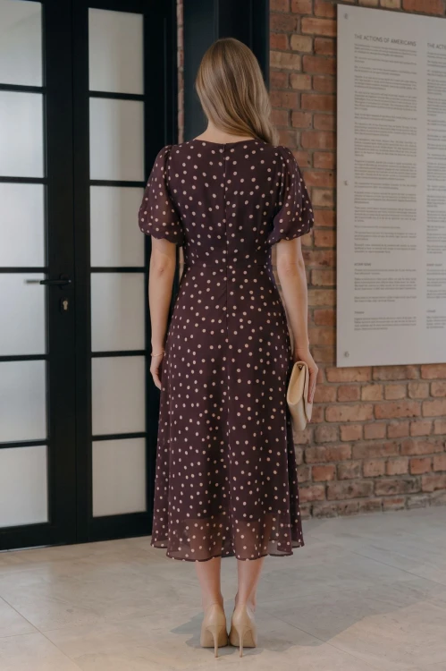 Na modelce stojącej tyłem elegancka sukienka w odcieniu burgundu, w beżowe groszki, okrągłym dekoltem, odcięciem lekko powyżej talii, krótkim, bufiastym rękawkiem zakończonym gumką, zapinana na plecach na długi, kryty suwak