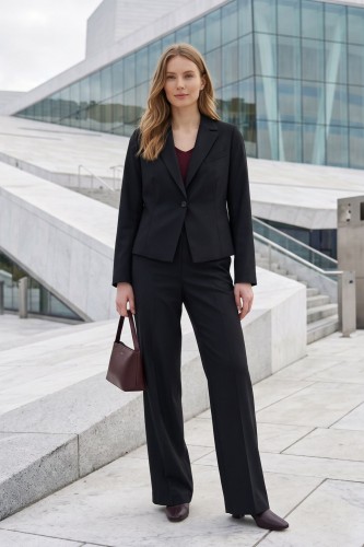 Na modelce stojącej przodem garnitur z wyłogami, w kolorze czarnym, zapinany na jeden guzik. Na przodzie po lewej stronie imitacja kieszonki oraz długie modelujące zaszewki, oraz szerokie spodnie na kant